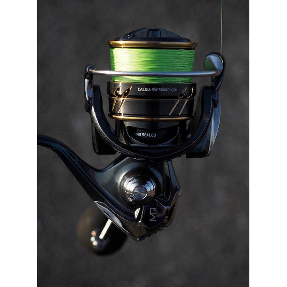 A fishing reel dark blue color with gold outlines and eva knob at the handle. The reel spool is full with green color braid.